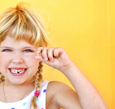 Happy,  blond Child holding tooth and smiling bright